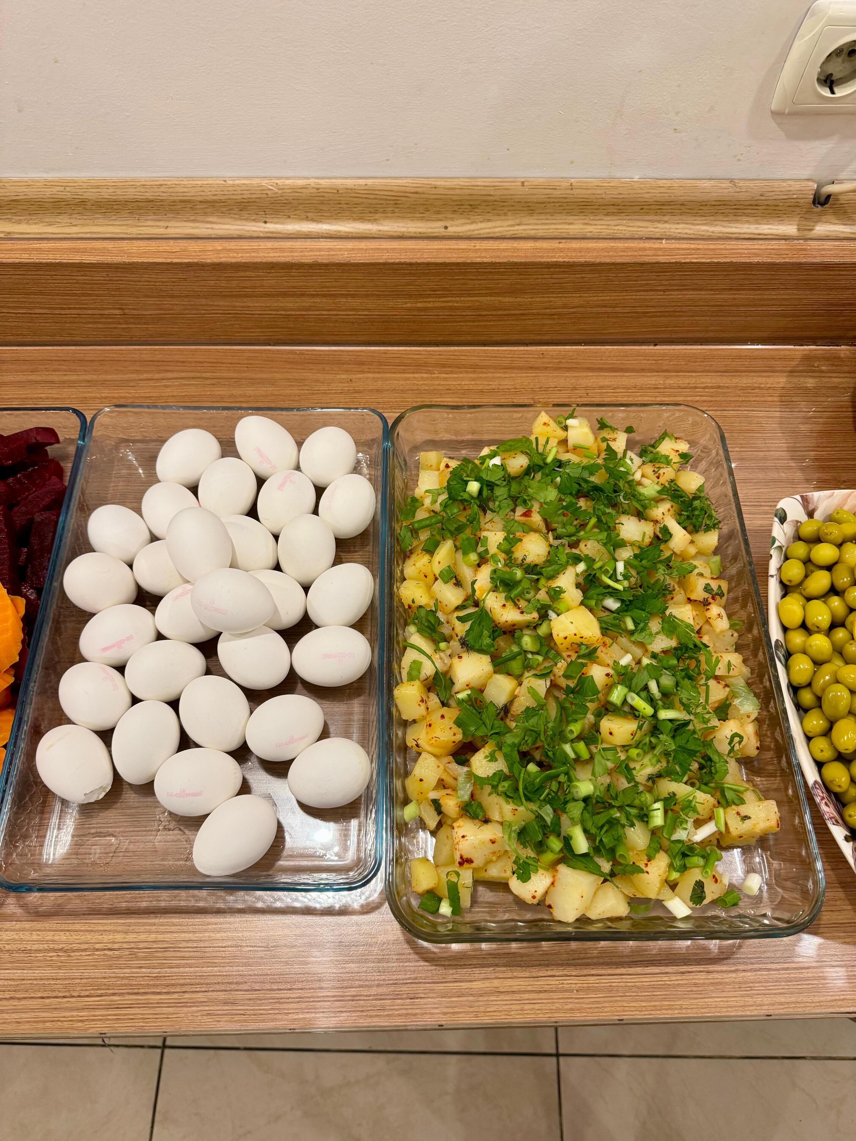 Une table de buffet avec trois plats en verre contenant des œufs, une salade de pommes de terre et des olives.