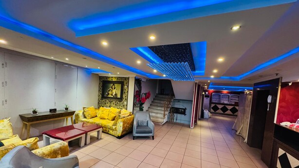 Un hall de hotel con un sofá amarillo, un sillón gris, una mesita y una escalera que sube a otro nivel.