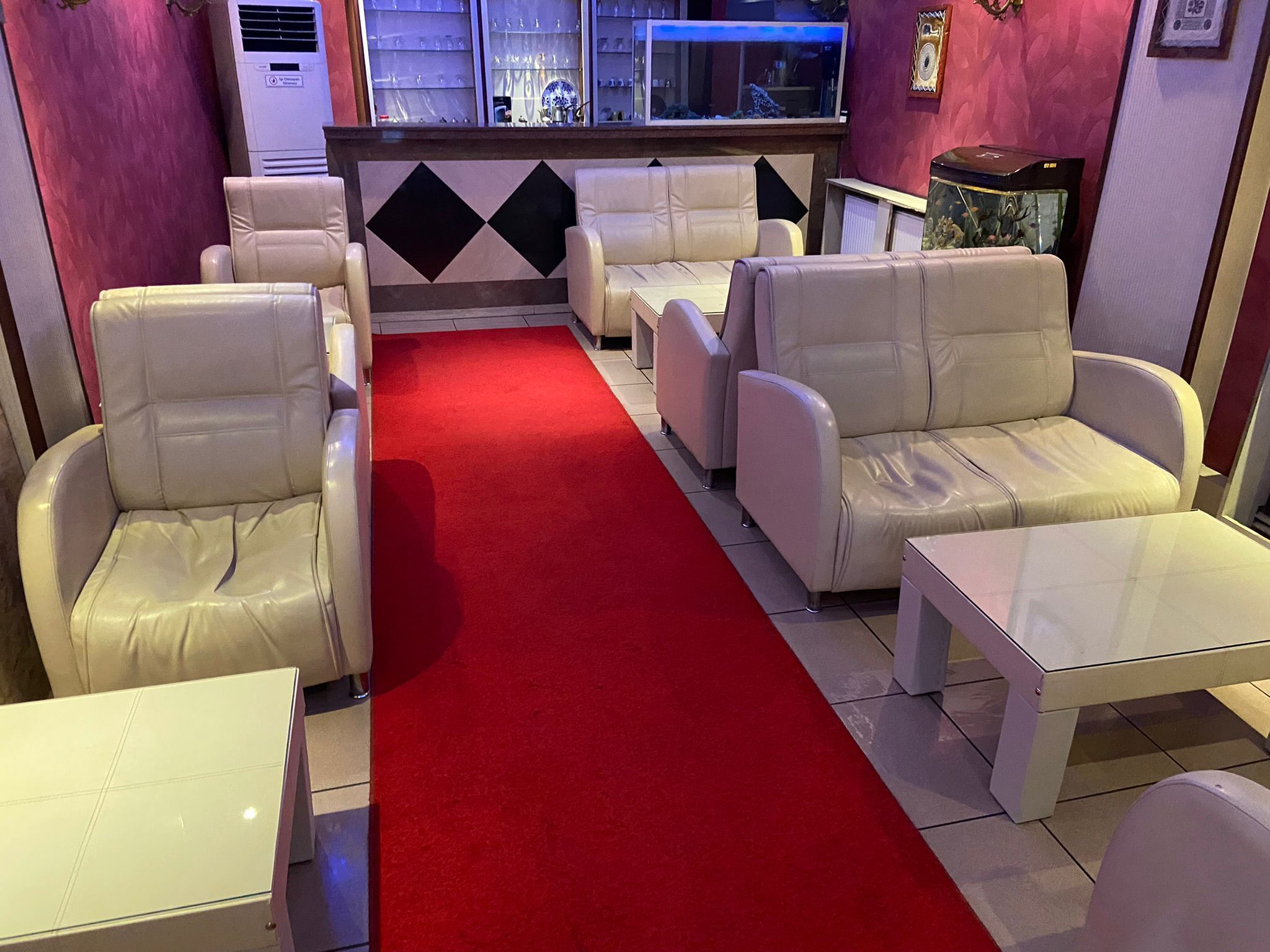Un vestíbulo de hotel con una alfombra roja que conduce a la recepción, rodeado de sofás y sillones de cuero blanco.