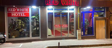 The exterior of the Red White Hotel with a prominent neon sign, glass doors, and a visible entrance.
