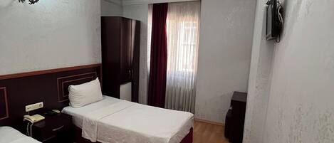 Habitación de hotel con dos camas, piso de madera, ventana con cortinas, teléfono en la pared y lámpara.