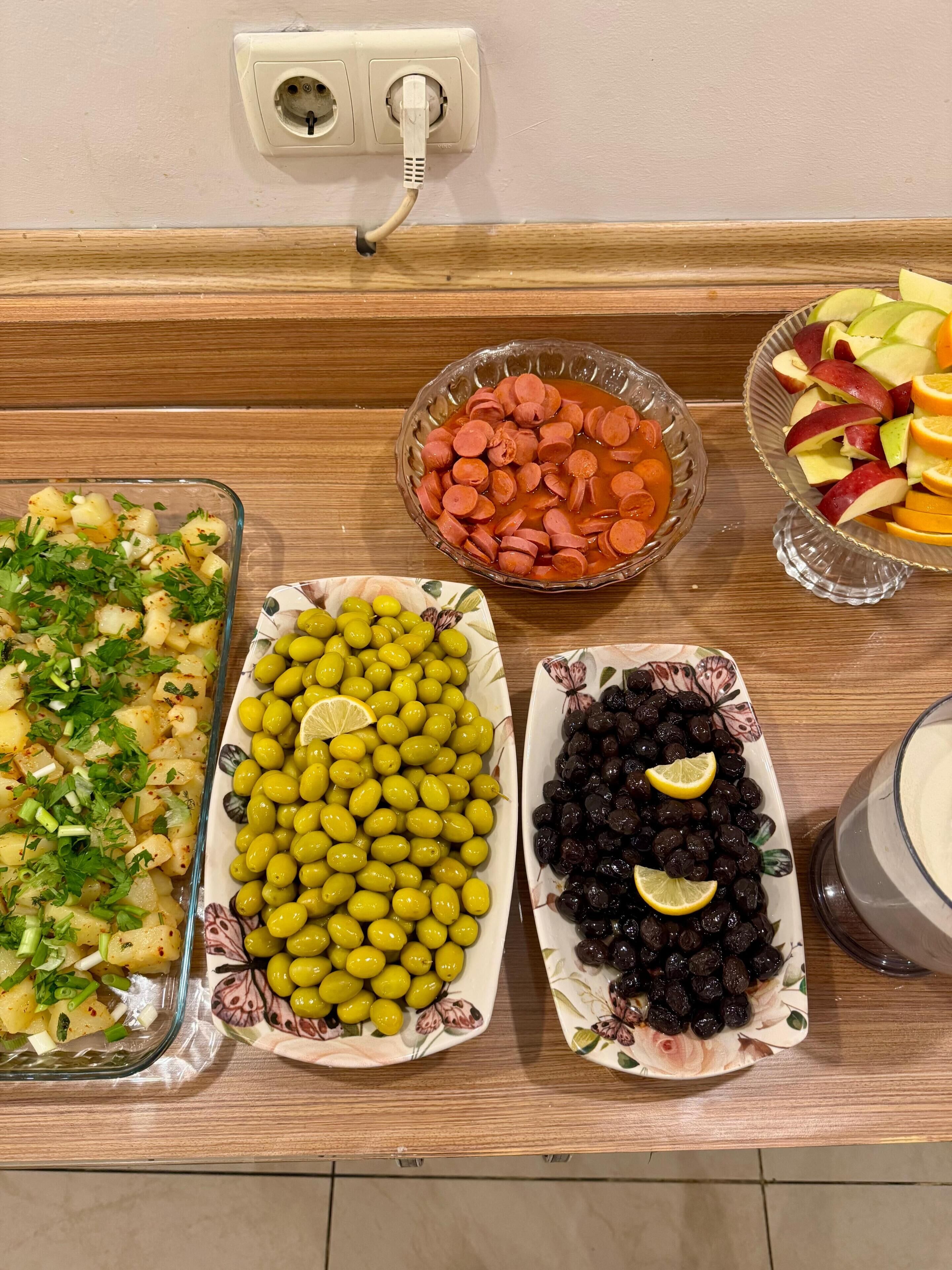 A buffet table with various dishes including potatoes, olives, and fruits.