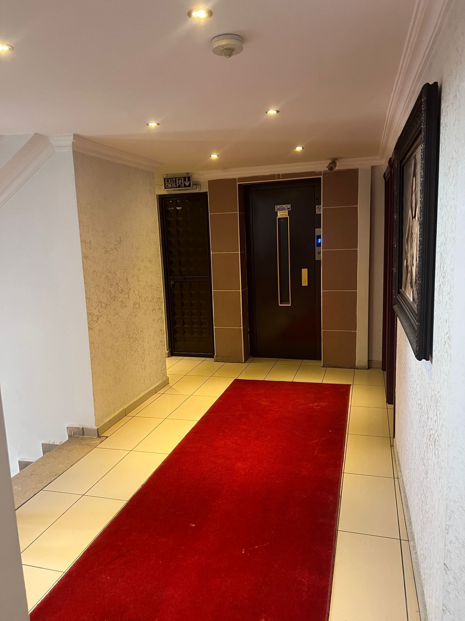 A hallway with a red carpet, two doors, and a sign indicating an exit.