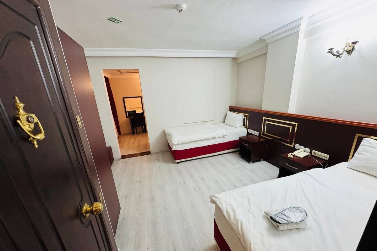 Une chambre d’hôtel avec une porte en bois, un lit avec du linge de lit blanc, une table de chevet avec une lampe et un petit bureau avec un téléphone.