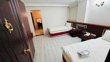 Une chambre d’hôtel avec une porte en bois, un lit avec du linge de lit blanc, une table de chevet avec une lampe et un petit bureau avec un téléphone.