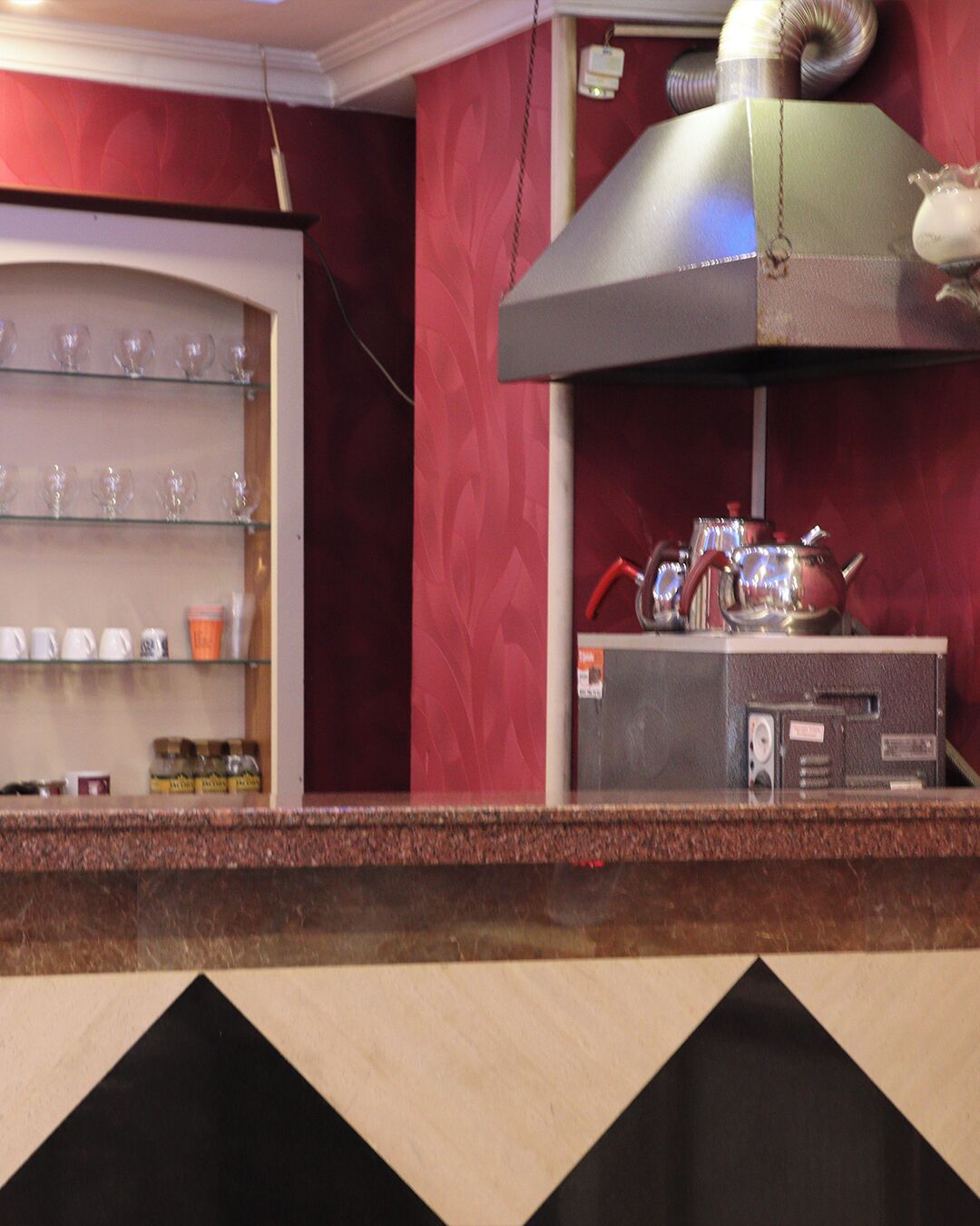 A kitchen area with a stainless steel range hood, a shelf with glassware, and a countertop with a kettle and pots.