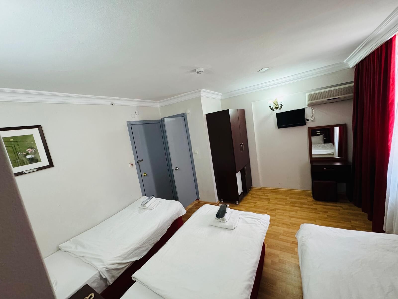 A hotel room with two single beds, a wardrobe, a mirror, a TV, and an air conditioning unit.