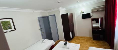 A hotel room with two single beds, a wardrobe, a mirror, a TV, and an air conditioning unit.