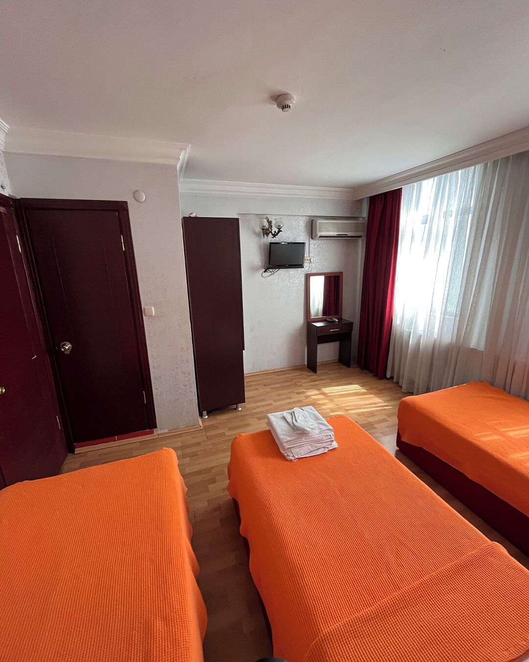 Une chambre d’hôtel avec deux lits orange, une armoire, un bureau avec un miroir et un appareil de climatisation.