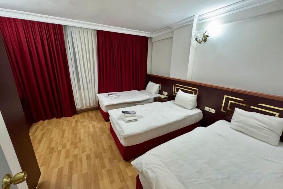 A hotel room with two beds, a wooden floor, and a red curtain.
