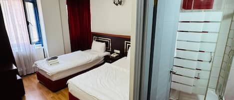 Habitación de hotel con dos camas, zona de ducha y vista al pasillo.