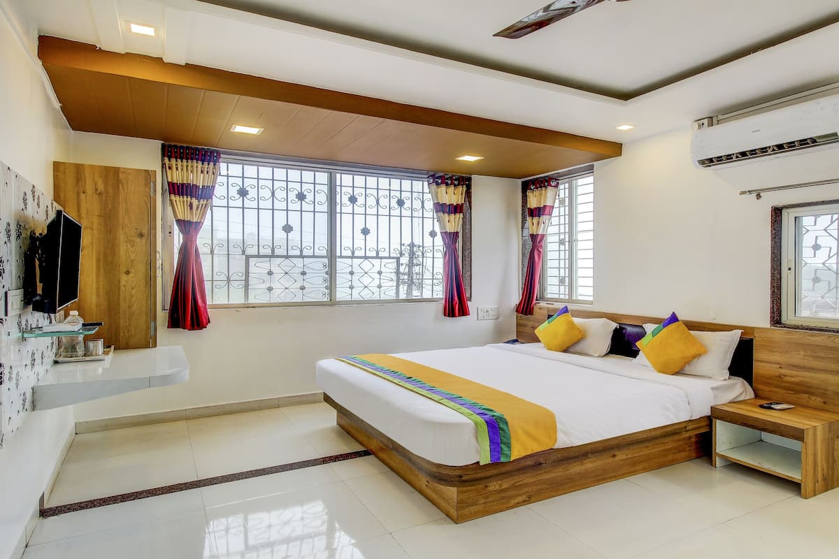 A bedroom with a wooden bed, a nightstand, a TV mounted on the wall, and a window with decorative curtains.