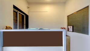 Een kamer met een groot bed, een raam met zonwering, een wandplank met boeken en een ingelijst kunstwerk aan de muur.