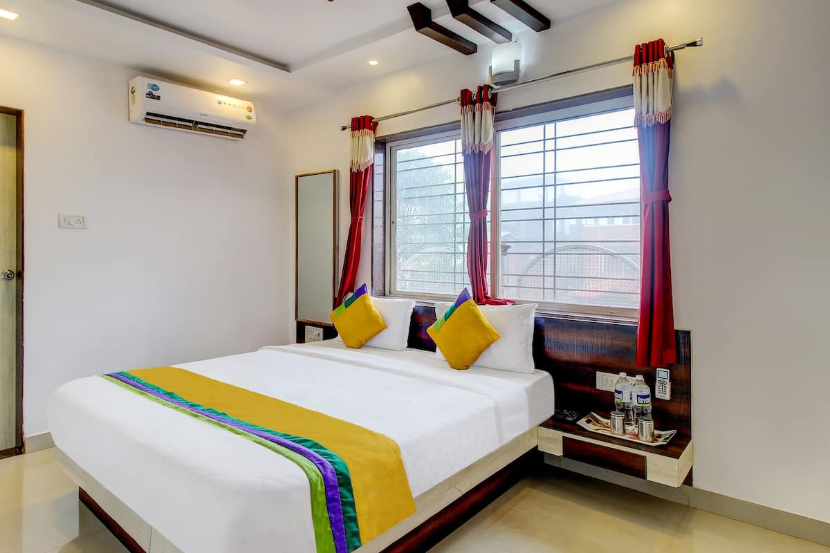A hotel room with a bed, bedside table, and a window with curtains.