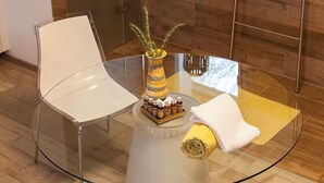 A modern bathroom with a glass table, white chairs, and a shower area.
