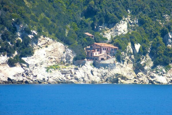 Une maison côtière avec un toit rouge, située sur une falaise rocheuse surplombant la mer.