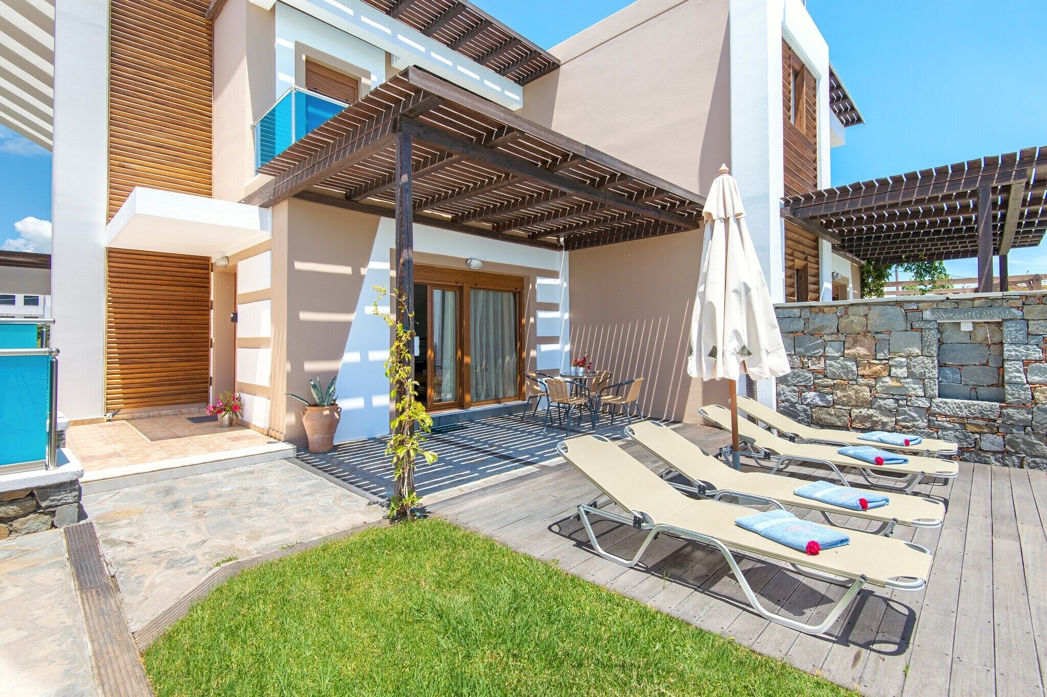 A modern outdoor pool area with lounge chairs, a stone wall, and a pergola.