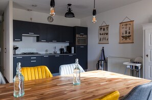 A modern kitchen with dark cabinets, a wooden dining table, and hanging light fixtures.
