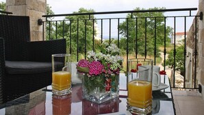 Un balcon avec une table préparée pour le petit-déjeuner, comprenant deux verres de jus d'orange, un vase avec des fleurs et une chaise en osier.