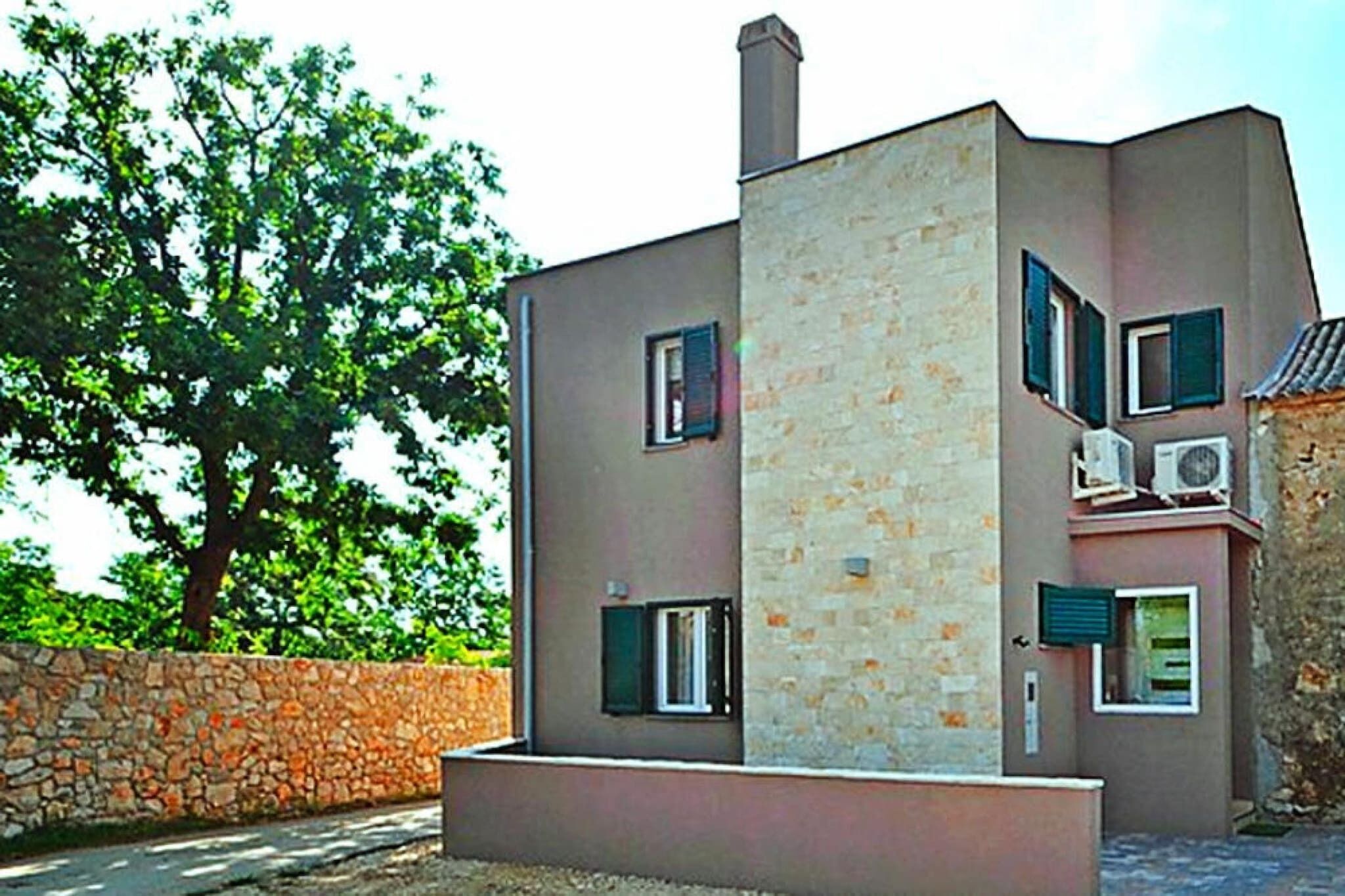 A modern two-story building with a stone facade, multiple windows, and an air conditioning unit on the exterior wall.