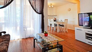 Un salon comprenant une table basse en verre, un canapé, un téléviseur et un coin repas avec des chaises et une table.