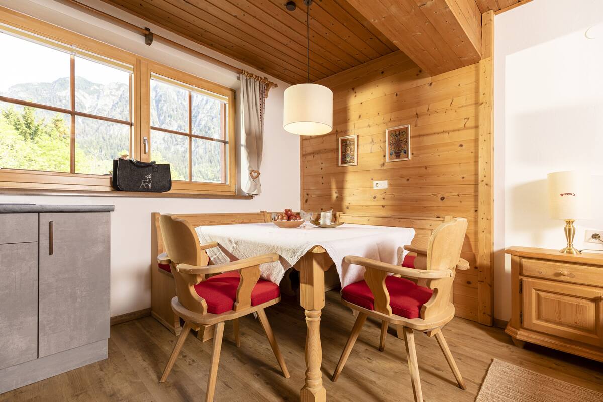 Interior de madera con una mesa de comedor, sillas, un armario y una ventana que ofrece vistas a las montañas.
