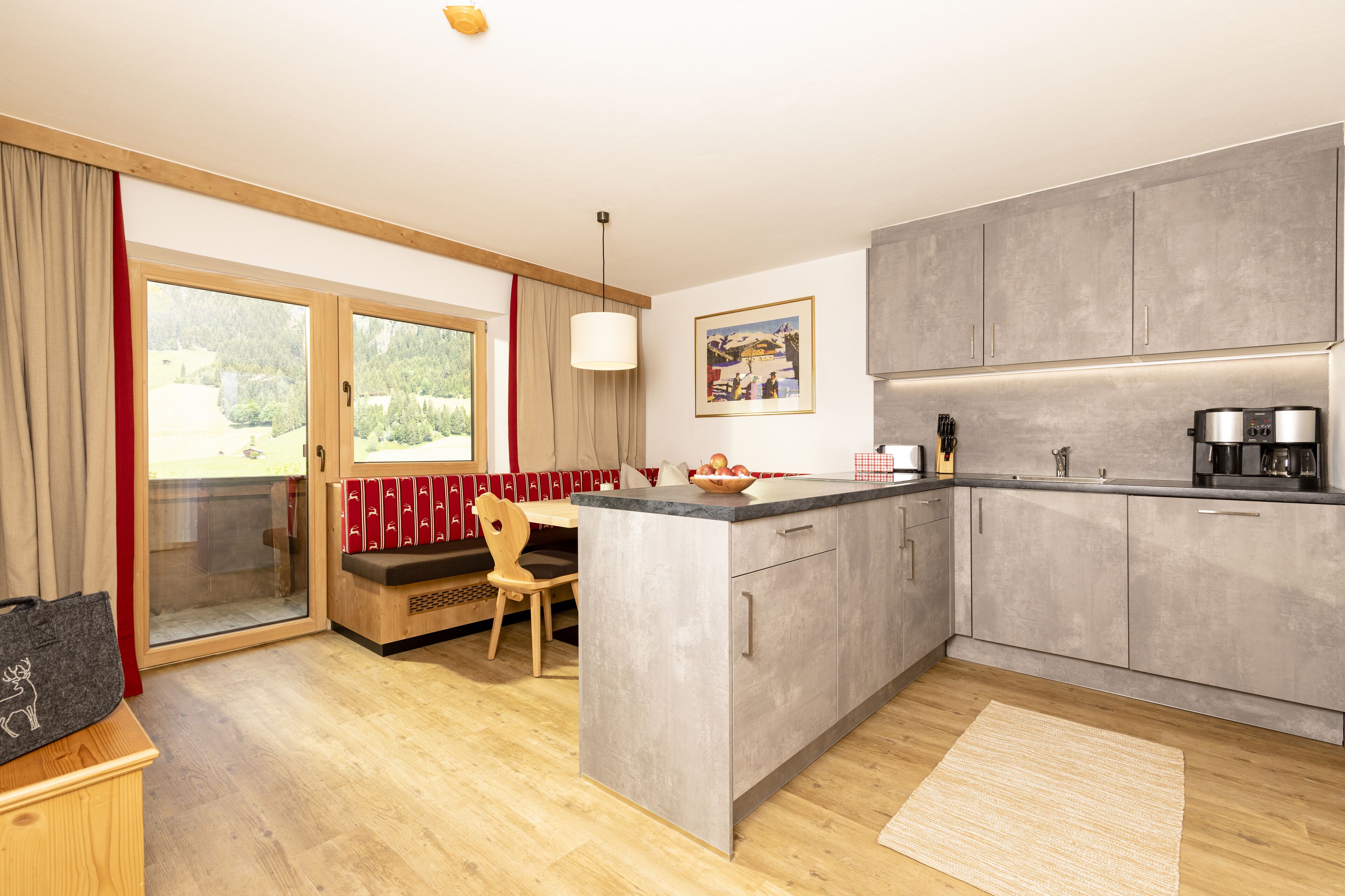 A modern kitchen with grey cabinets, a wooden dining table, and a large window with a view of the outdoors.