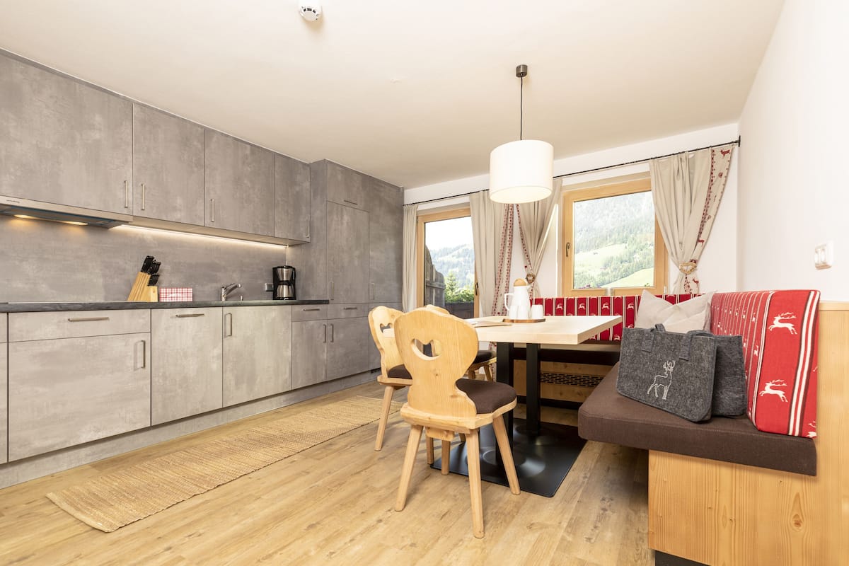 Una cocina moderna con armarios grises, una mesa de comedor de madera y un banco con bolsas de almacenamiento.