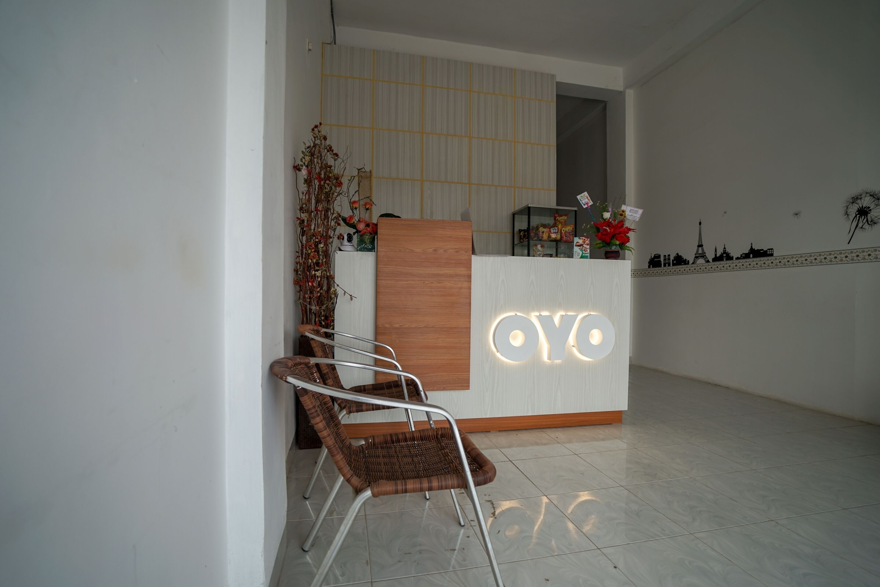 Un comptoir d’accueil avec un panneau en bois et le nom « OYLO » illuminé. Deux fauteuils en osier sont placés devant.