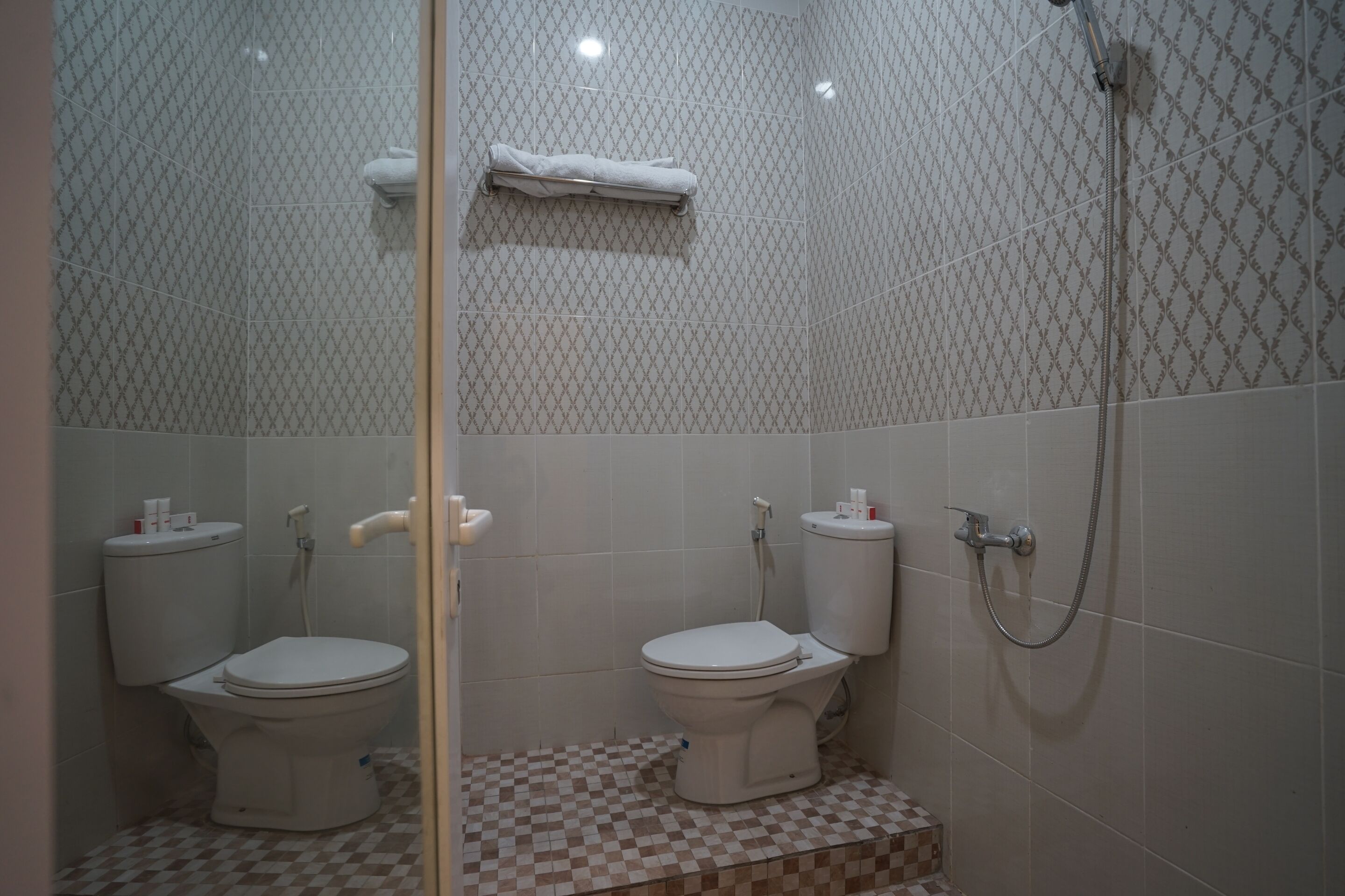 Een badkamer met twee toiletten, een douche en een zwart-wit betegelde vloer.