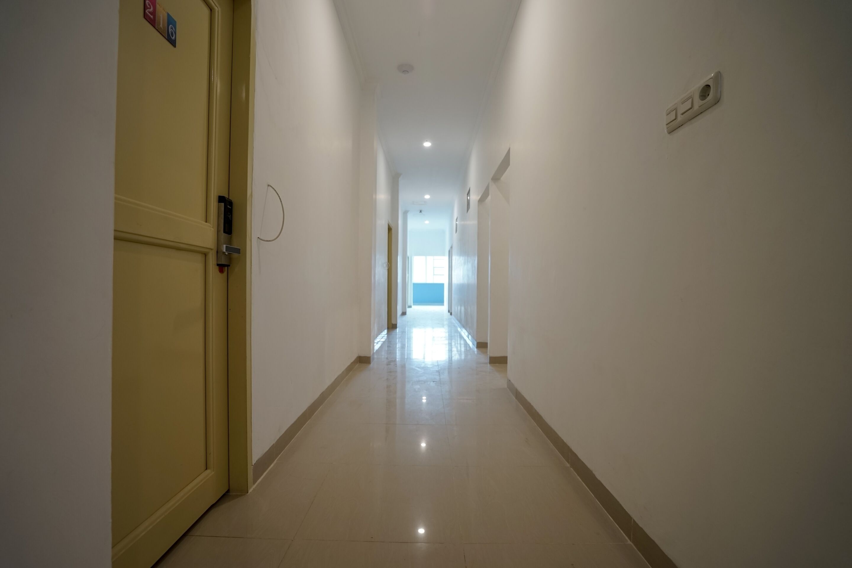 A long, narrow hallway with a door on the left and a light switch on the right.