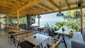 An outdoor dining area with wooden tables and chairs, a wooden ceiling, and a view of the sea.