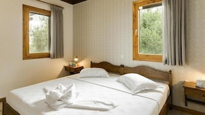 A bedroom with two beds, wooden headboards, and curtains over windows.