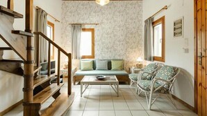 A cozy living room with a wooden staircase, a sofa with cushions, a coffee table, and wicker chairs.