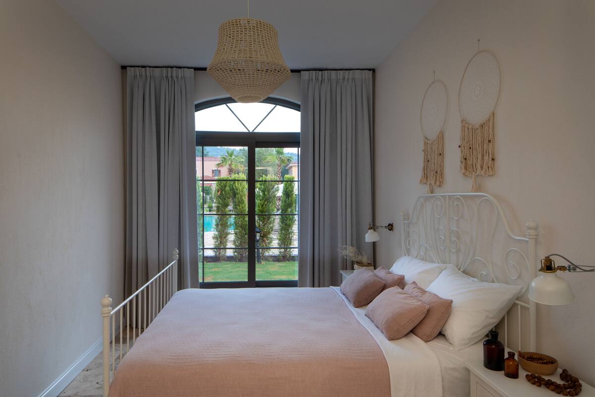A bedroom with a large bed, a window with curtains, a bedside lamp, and a wall with dreamcatchers.