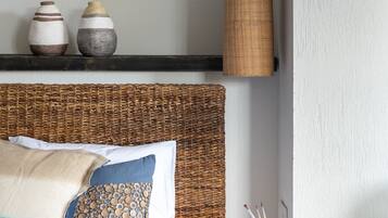 Un dormitorio ordenado con cama, almohadas, una mesita de noche, un estante en la pared con objetos decorativos y una lámpara colgante.