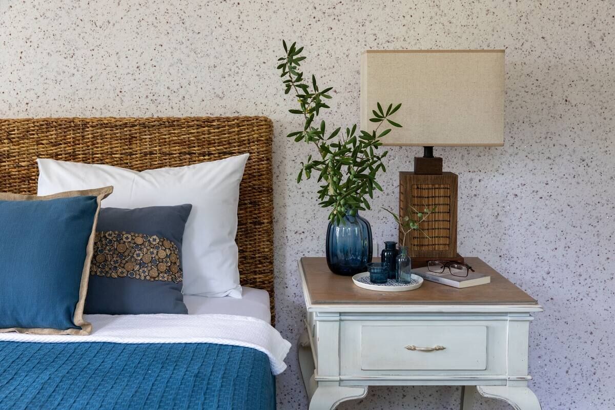 A bedroom with a bed, pillows, a bedside table with a lamp, and a wall-mounted shelf.