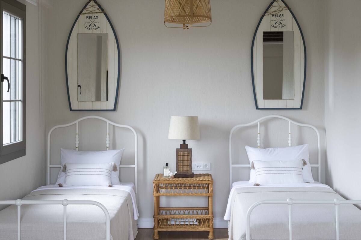 A bedroom with two beds, a nightstand, and two wall mirrors.