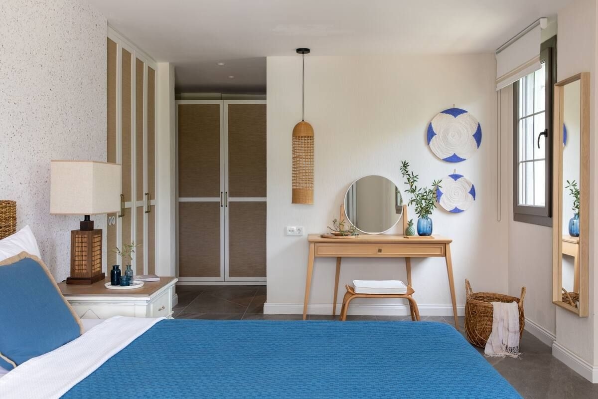 A bedroom with a bed, bedside table, dresser, vanity, mirror, and a desk with a chair.
