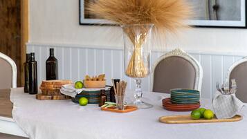 A dining table with a white tablecloth, a vase with dried plants, and various food items. There are framed artworks on the wall behind the table.