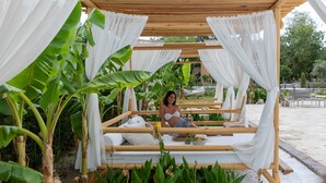 Estructura de cama de madera con cortinas blancas, rodeada de exuberante follaje y plantas de plátano.