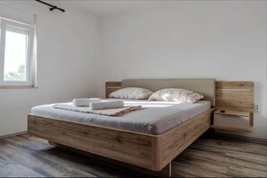 A modern bedroom with a wooden bed frame, a bedside table, and a window with a view.