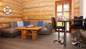 A log cabin interior with a wooden table, two bar stools, a sofa with cushions, and a door leading outside. - Blockhaus in Trassenheide (Trassenheide)
