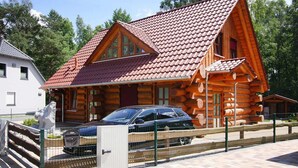 A log cabin with a red-tiled roof, a car parked in front, and a fenced area. - Blockhaus in Trassenheide (Trassenheide)