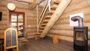 A log cabin interior with a wooden staircase, a dining table with chairs, and a wood-burning stove. - Blockhaus in Trassenheide (Trassenheide)