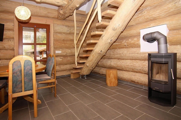 A log cabin interior with a wooden staircase, a dining table with chairs, and a wood-burning stove. - Blockhaus in Trassenheide (Trassenheide)