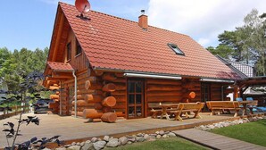 A log cabin with a red-tiled roof, wooden exterior, and a deck with picnic tables. - Blockhaus in Trassenheide (Trassenheide)