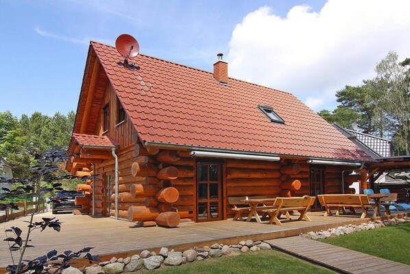 A log cabin with a red-tiled roof, wooden exterior, and a deck with picnic tables.