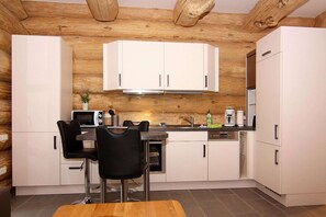 A modern kitchen with white cabinets, a wooden ceiling, and a dining area with black chairs.