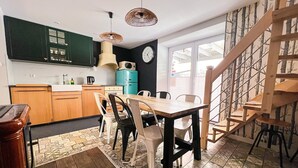 A kitchen with wooden cabinets, a dining table with chairs, a clock on the wall, and a staircase.